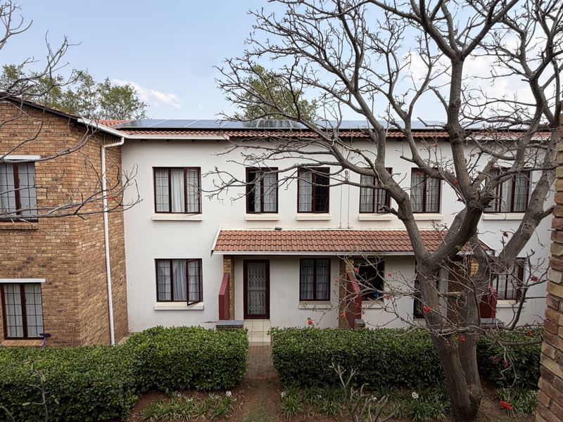 A rear view of a two-story apartment building featuring a brick and plaster facade, tiled roof, and installed solar panels.