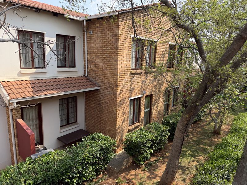 A view of the rear elevation of a two-story apartment building featuring face brick and plastered walls, tiled roofing, and a landscaped garden area.