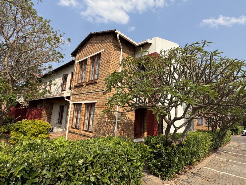 A well-maintained apartment building exterior featuring classic face brick construction, timber window frames, and established garden landscaping with a paved driveway.