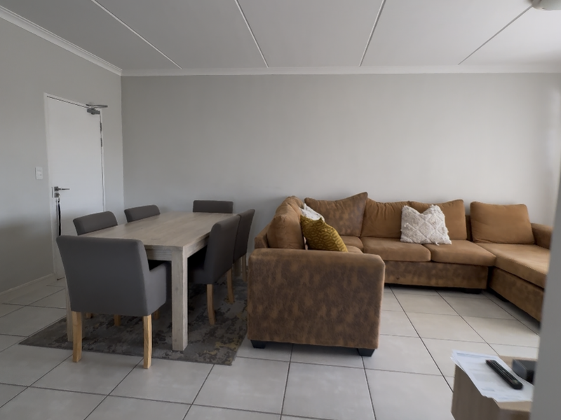 Open-plan living and dining area featuring neutral wall tones and light-colored floor tiles, providing a versatile space for relaxation and meals.