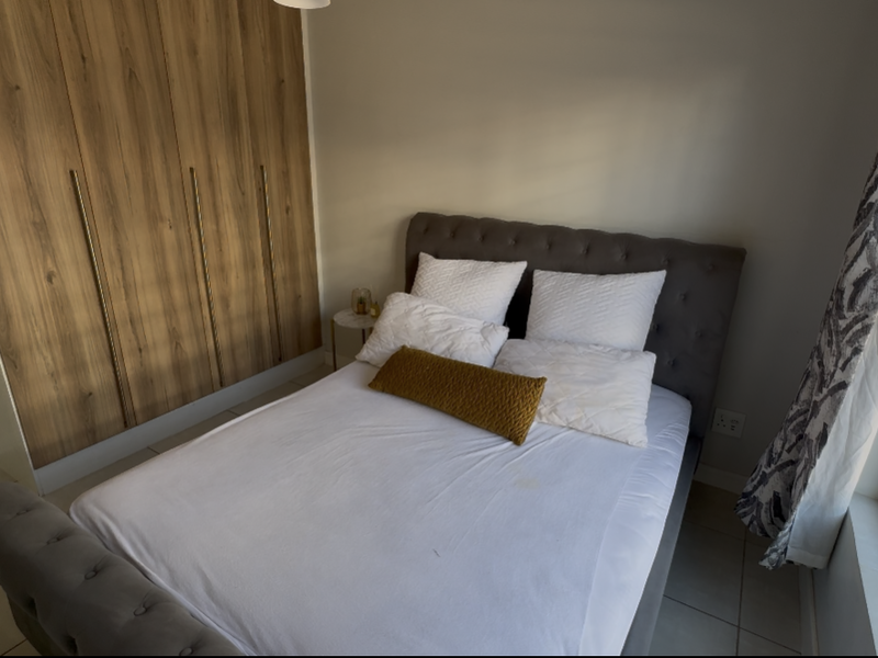 A well-maintained bedroom featuring modern wood-finish built-in cupboards, neutral tiled flooring, and a large window allowing for natural light.