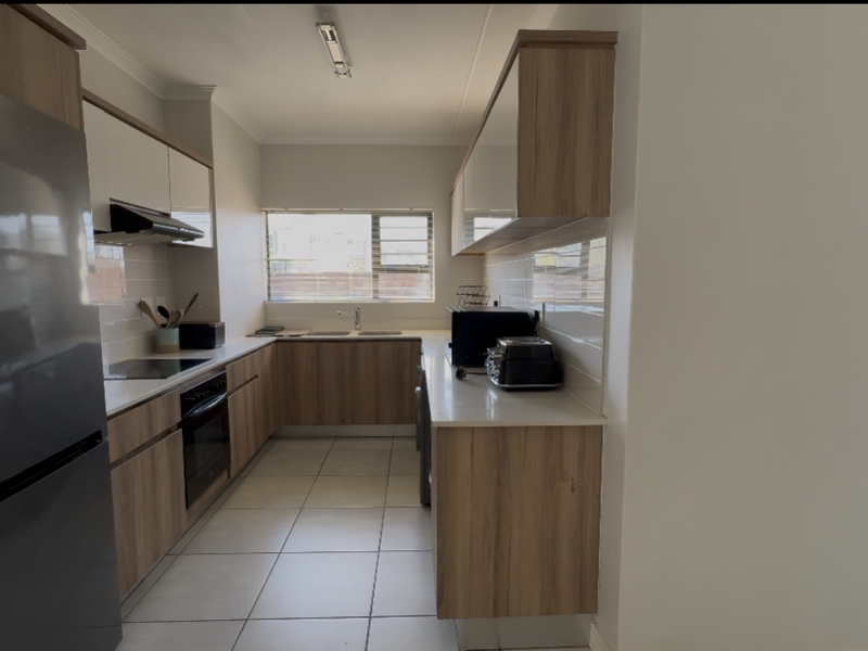 Modern kitchen featuring wood-finish cabinetry, stone countertops, built-in oven, electric hob, and tiled flooring with ample natural light.