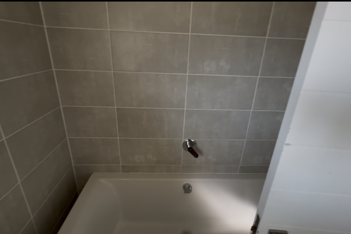 A clean bathroom space featuring a built-in bathtub with neutral wall tiling and modern chrome fixtures.