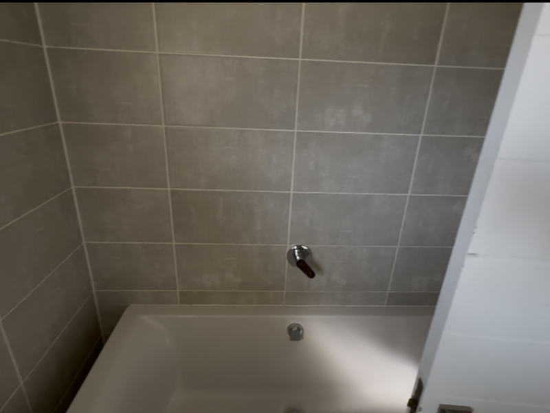 A clean bathroom space featuring a built-in bathtub with neutral wall tiling and modern chrome fixtures.
