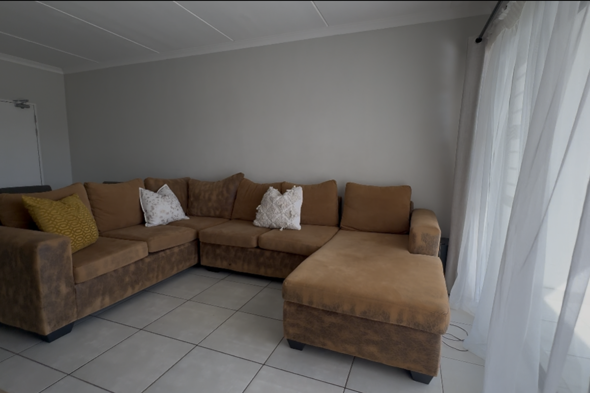 A living room area featuring neutral tiled flooring and a large sliding glass door with sheer curtains, providing access to the exterior.
