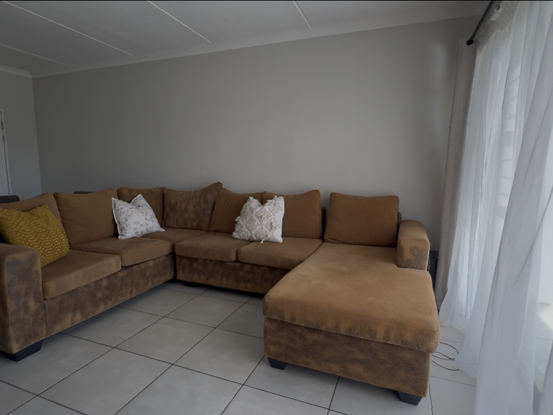 A living room area featuring neutral tiled flooring and a large sliding glass door with sheer curtains, providing access to the exterior.