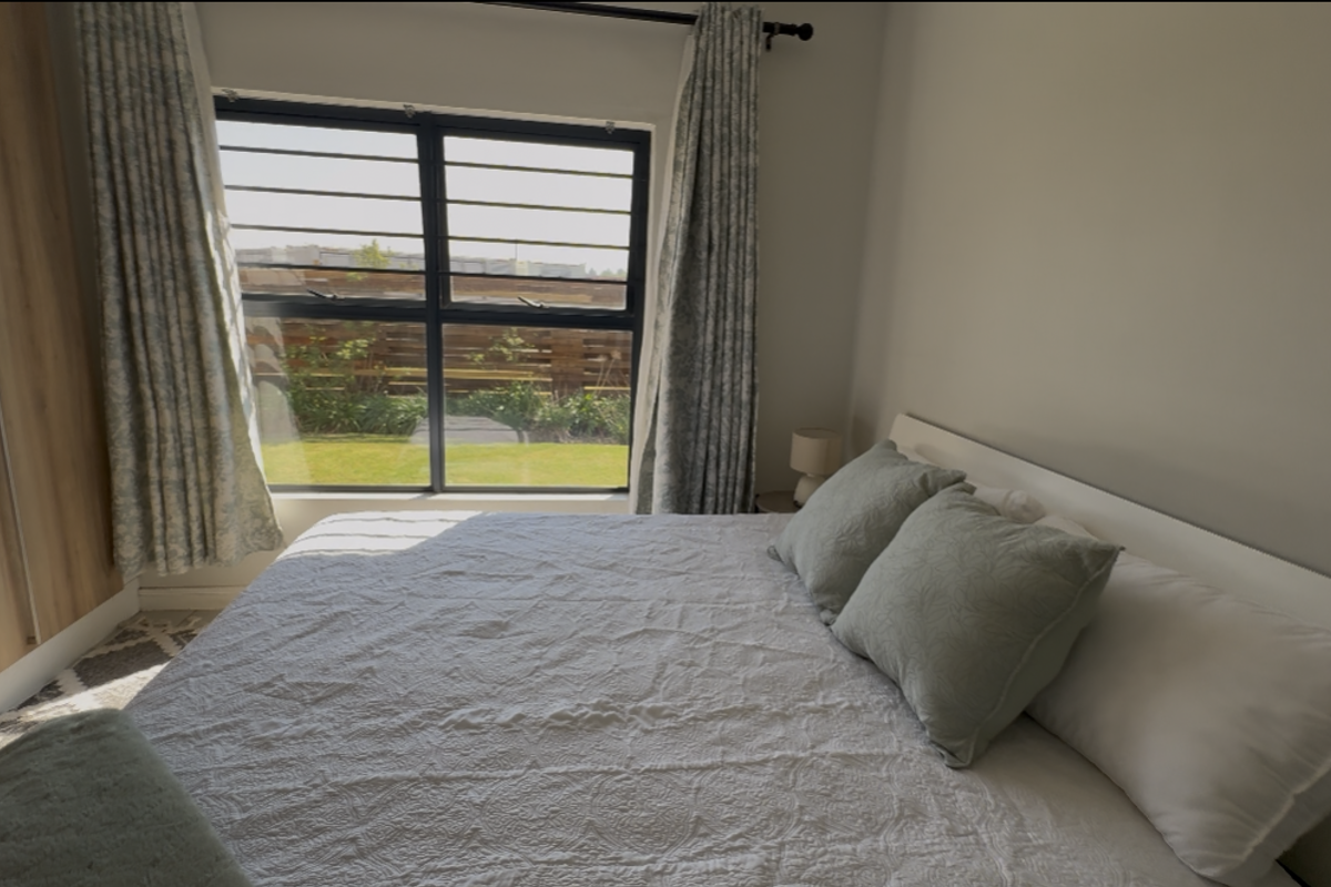 A well-lit bedroom featuring a built-in wardrobe, large window with security bars, and views of the garden.