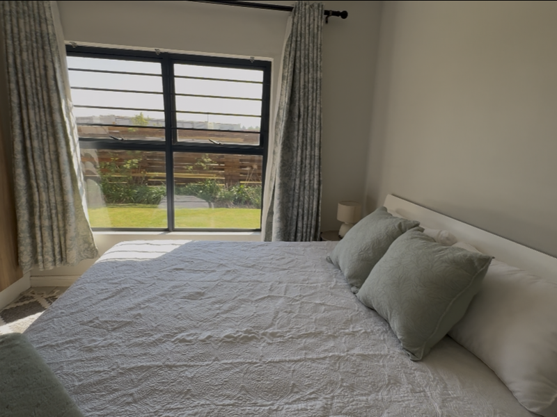A well-lit bedroom featuring a built-in wardrobe, large window with security bars, and views of the garden.