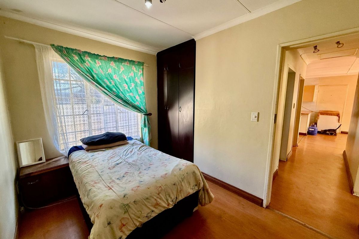 A bedroom featuring built-in dark wood cabinetry, a window with security bars, and access to an adjacent hallway.