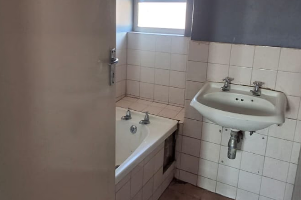 A dated bathroom featuring a wall-mounted basin and a bathtub with tiled surrounds, requiring cosmetic updates and repairs to the bathtub panel.