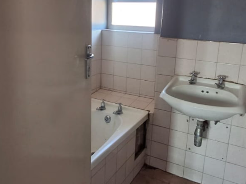 A dated bathroom featuring a wall-mounted basin and a bathtub with tiled surrounds, requiring cosmetic updates and repairs to the bathtub panel.