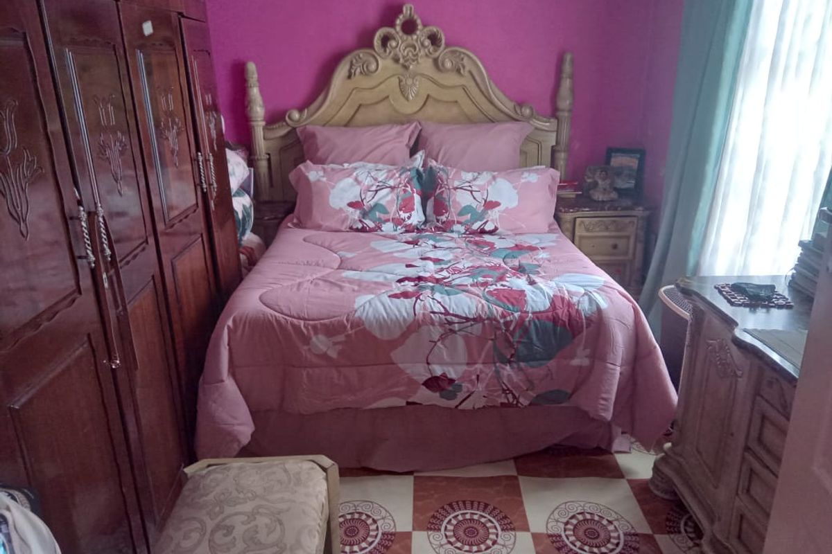 A bedroom featuring a built-in wooden wardrobe and patterned floor tiles, requiring cosmetic updates to modernize the space.