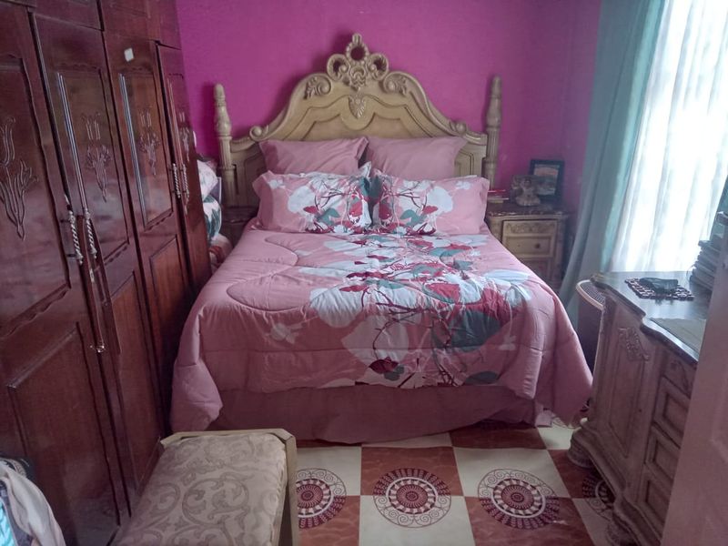 A bedroom featuring a built-in wooden wardrobe and patterned floor tiles, requiring cosmetic updates to modernize the space.