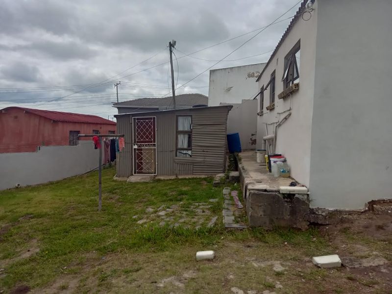 Rear view of the property showing a corrugated metal outbuilding, a concrete walkway, and the rear elevation of the main house structure.