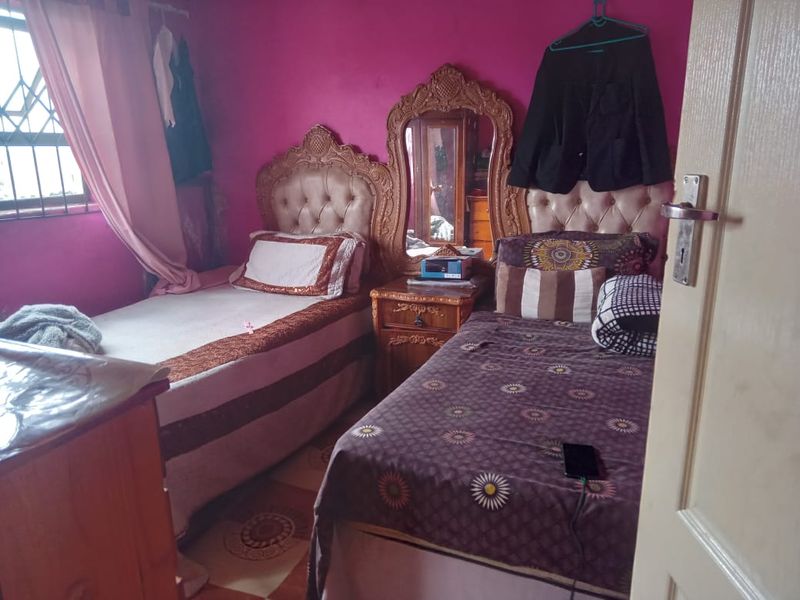 A bedroom featuring tiled flooring and security bars on the window, currently furnished with twin beds.