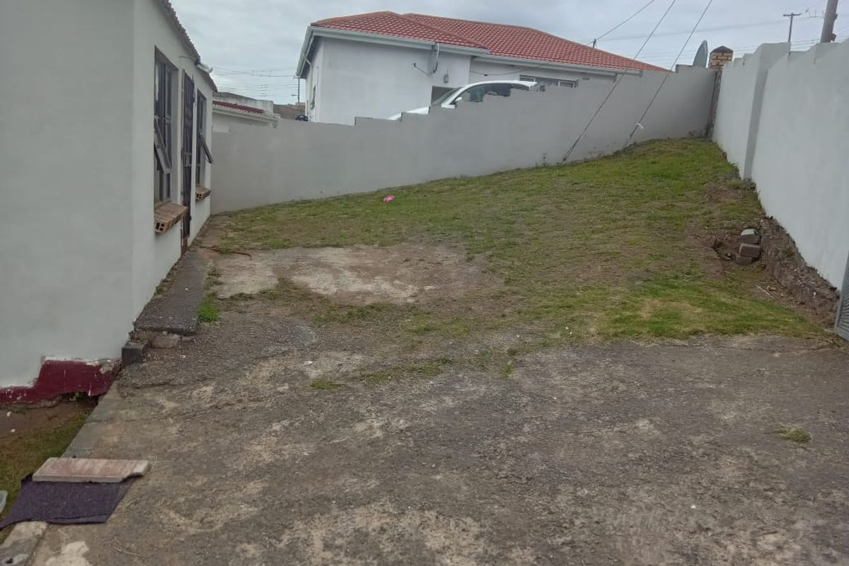 A rear exterior area featuring a concrete paved section and a sloped lawn enclosed by perimeter boundary walls.