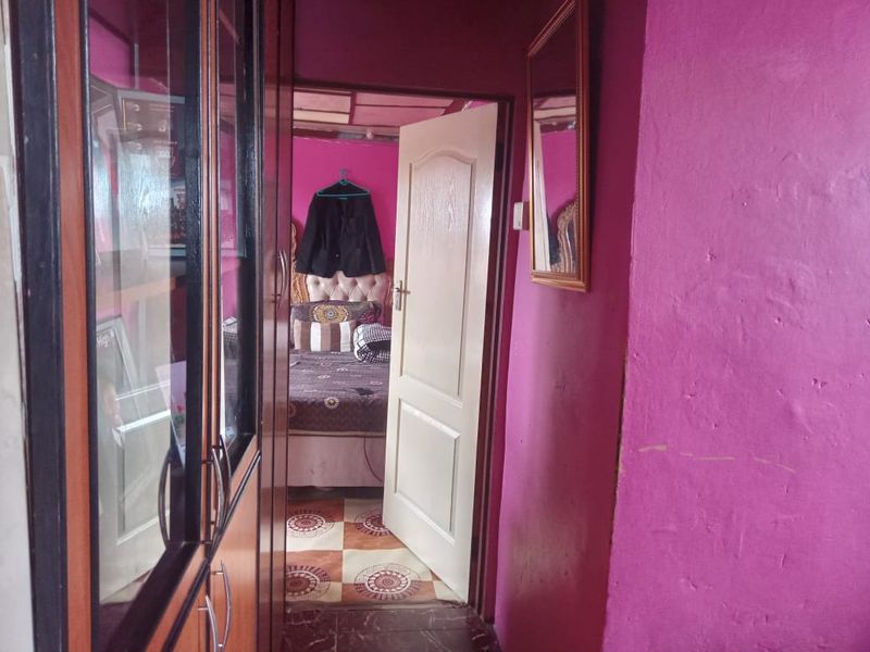 A narrow hallway featuring built-in storage cupboards and access to an adjacent bedroom with tiled flooring.