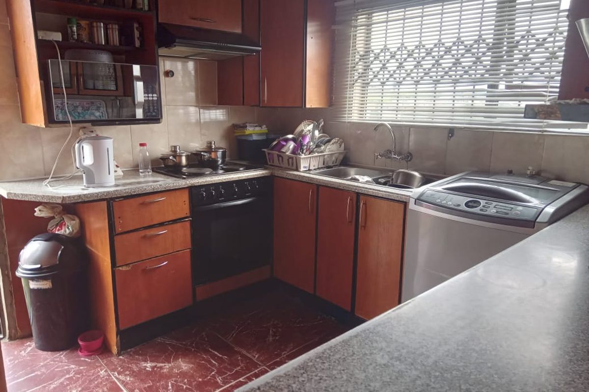 A functional kitchen featuring wood-look laminate cabinetry, built-in oven and hob, tiled backsplash, and a stainless steel sink with window security gate.