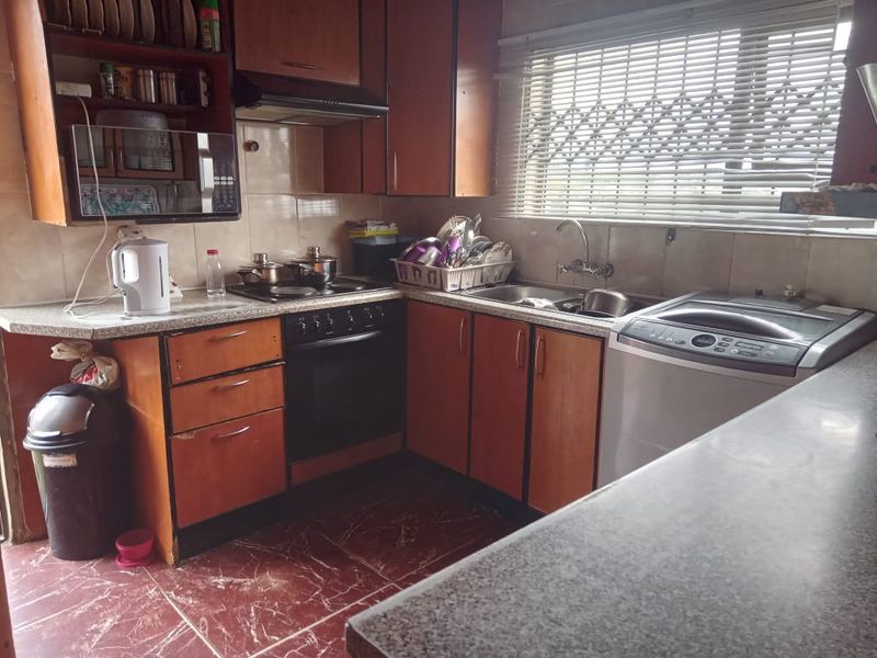 A functional kitchen featuring wood-look laminate cabinetry, built-in oven and hob, tiled backsplash, and a stainless steel sink with window security gate.