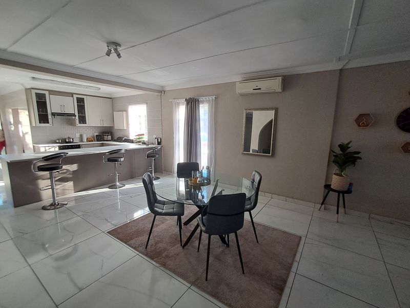 Open-plan living and dining area featuring modern tiled flooring, a breakfast bar, and a functional kitchen with built-in cabinetry and an extractor fan.