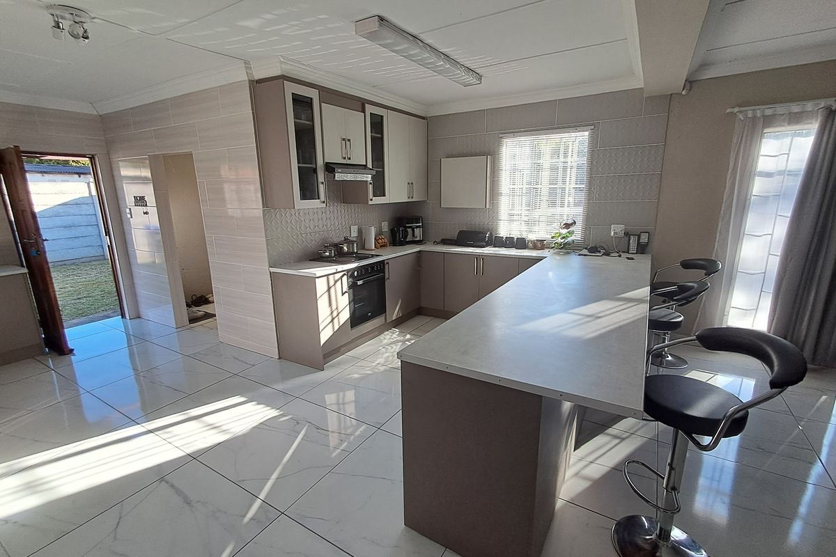 Modern kitchen featuring sleek cabinetry, a central island with breakfast bar seating, tiled flooring, and integrated appliances, offering a bright and functional cooking space.