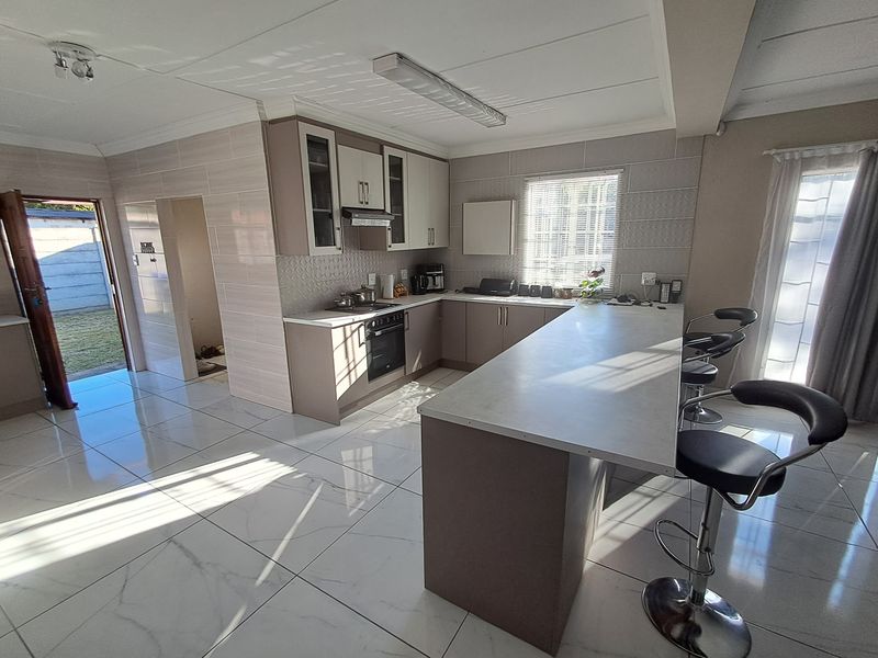 Modern kitchen featuring sleek cabinetry, a central island with breakfast bar seating, tiled flooring, and integrated appliances, offering a bright and functional cooking space.