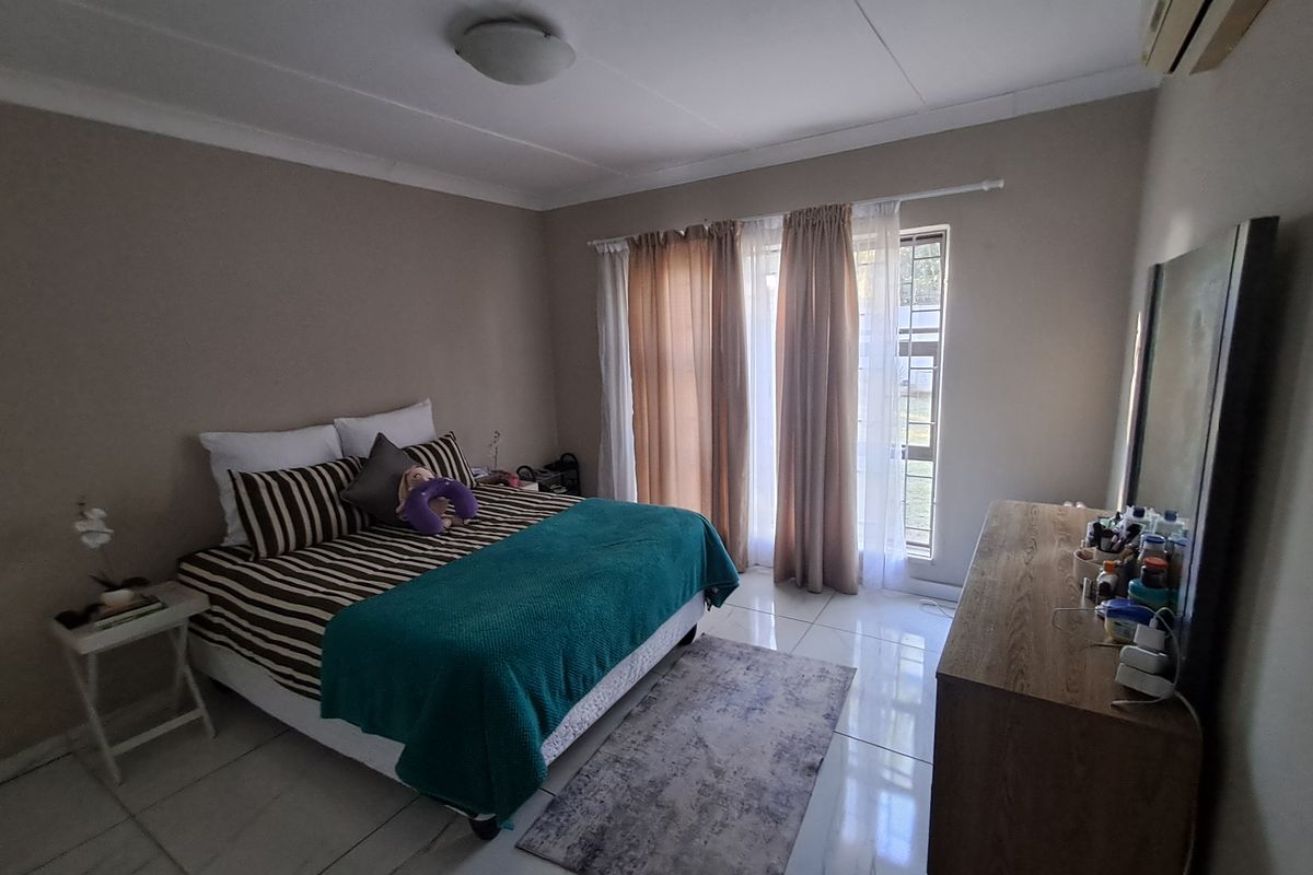 A functional bedroom featuring tiled flooring, an integrated air conditioning unit, and large windows with curtain rails for natural light.