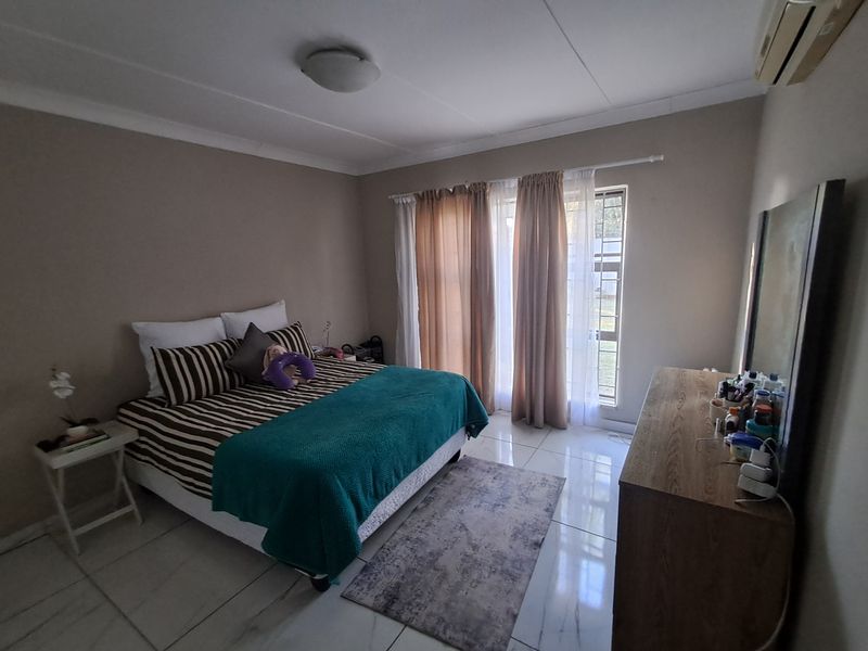 A functional bedroom featuring tiled flooring, an integrated air conditioning unit, and large windows with curtain rails for natural light.