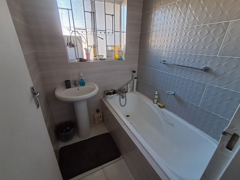 A compact bathroom featuring a pedestal basin, a bathtub with a handheld shower mixer, and neutral wall tiling.