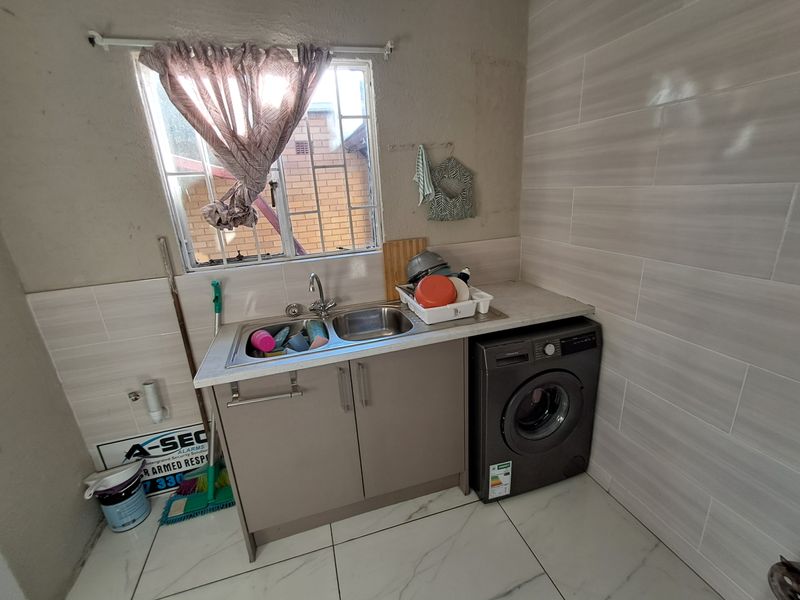 A functional laundry area featuring a stainless steel sink, built-in cabinetry, and tiled finishes, providing a practical space for household utility tasks.