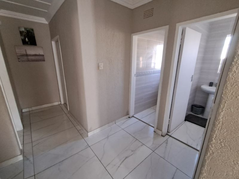 A bright hallway featuring marble-look tiled flooring, leading into a bathroom area with a pedestal basin.