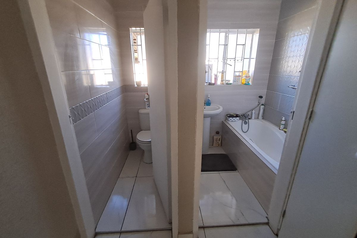 A functional bathroom featuring a separate toilet area, pedestal basin, and bathtub with neutral wall and floor tiling.