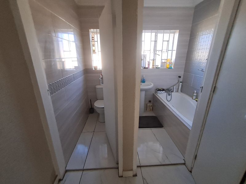 A functional bathroom featuring a separate toilet area, pedestal basin, and bathtub with neutral wall and floor tiling.