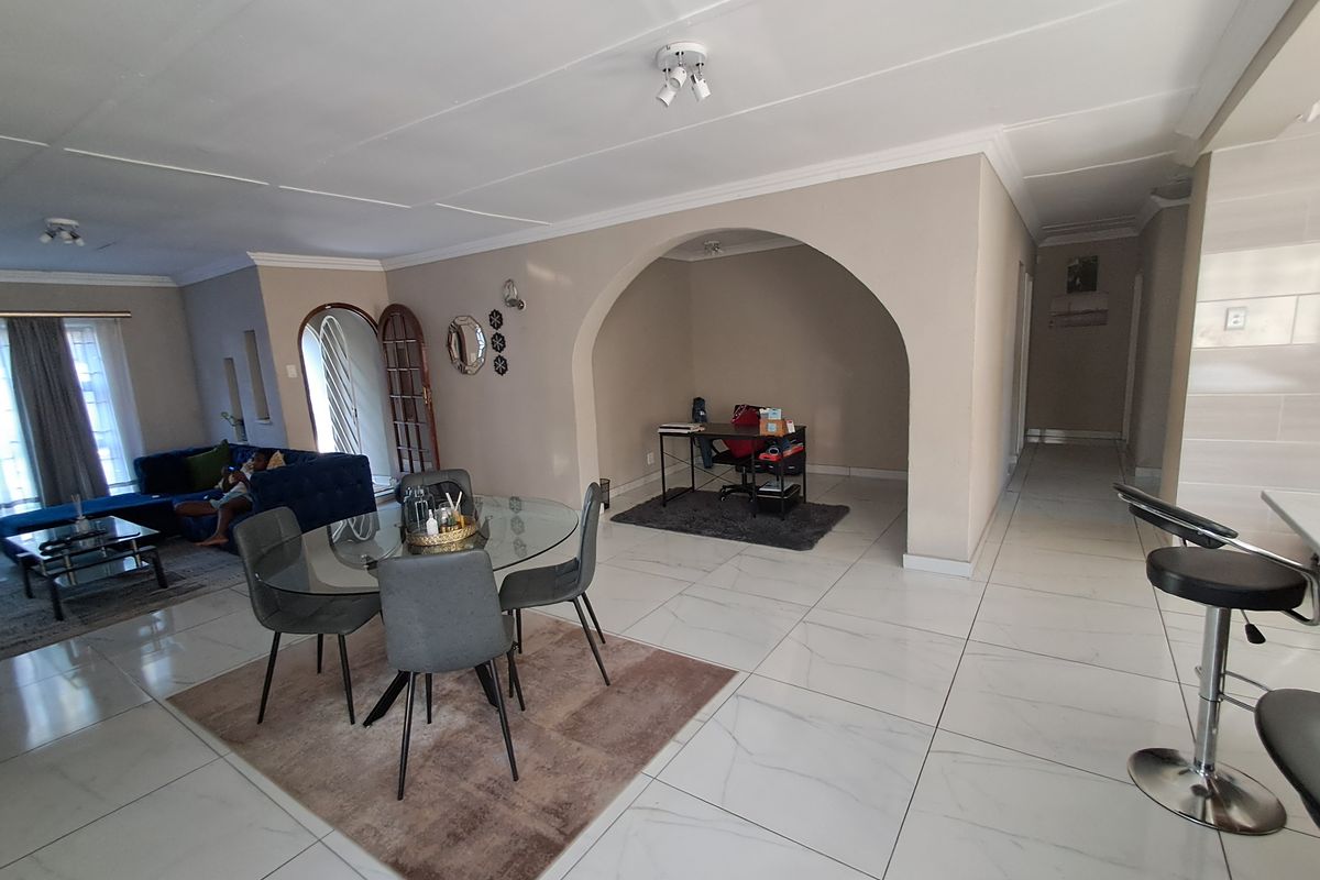 Spacious open-plan living and dining area featuring large format floor tiles, a distinctive arched alcove, and neutral wall finishes.