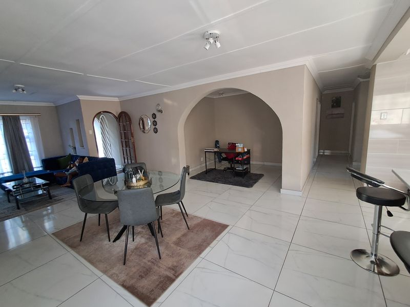 Spacious open-plan living and dining area featuring large format floor tiles, a distinctive arched alcove, and neutral wall finishes.