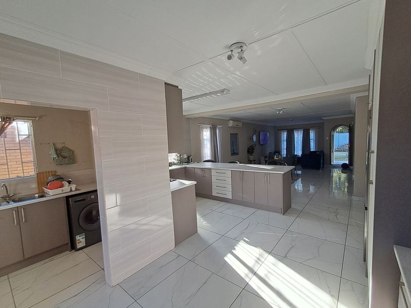 Spacious open-plan living area featuring a modern kitchen with a central island, tiled flooring, and an adjoining scullery area.