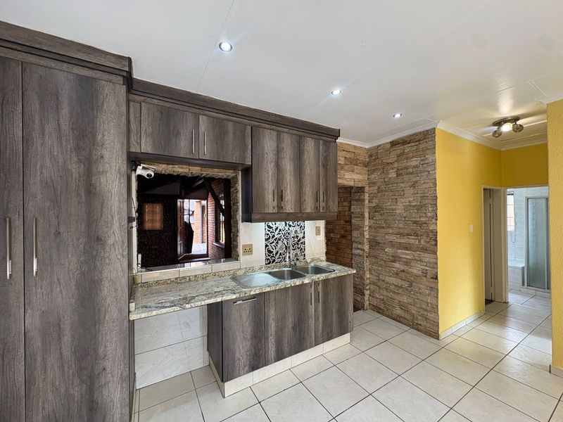 A functional kitchen featuring dark wood-look cabinetry, granite countertops, a double sink, and a decorative stone veneer feature wall with tiled flooring.