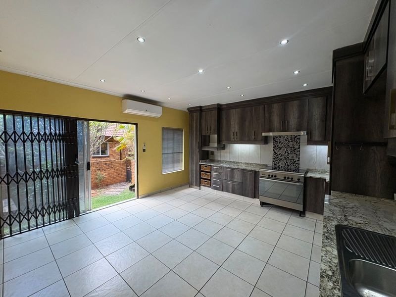 Modern kitchen featuring dark wood cabinetry, granite countertops, stainless steel stove, and direct access to the rear garden through a sliding glass door.