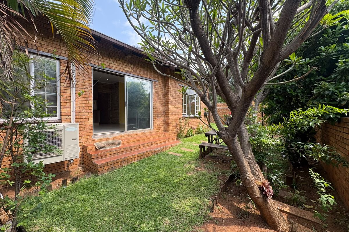 Rear view of a face brick townhouse featuring a sliding glass door entrance, brick steps, and an external air conditioning unit set within a garden.