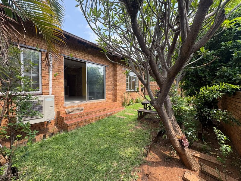 Rear view of a face brick townhouse featuring a sliding glass door entrance, brick steps, and an external air conditioning unit set within a garden.