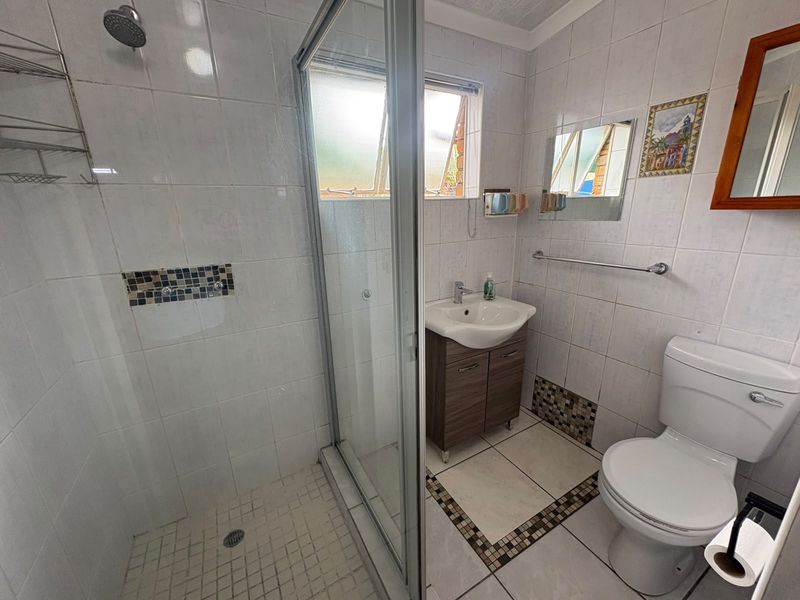 A functional bathroom featuring a glass-enclosed shower, a vanity unit with a basin, and a standard toilet with tiled finishes throughout.