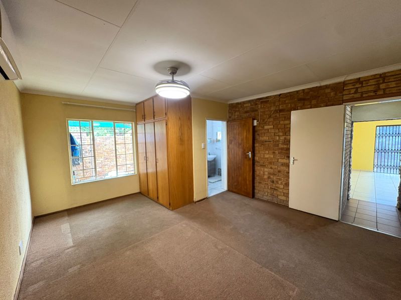 Spacious bedroom featuring built-in cupboards, an exposed brick feature wall, and a ceiling fan, offering a blank canvas for personalization.