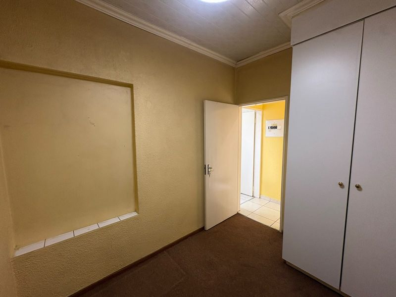 An empty bedroom featuring a built-in wardrobe, a recessed wall niche, and carpeted flooring, leading into a tiled hallway.