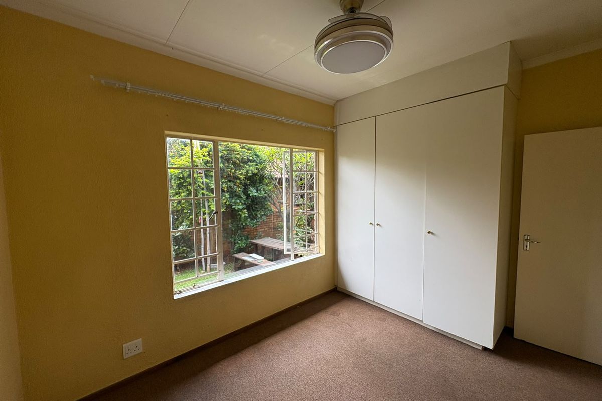 A vacant bedroom featuring built-in cupboards, a ceiling fan, and carpeted flooring with a view of the garden.