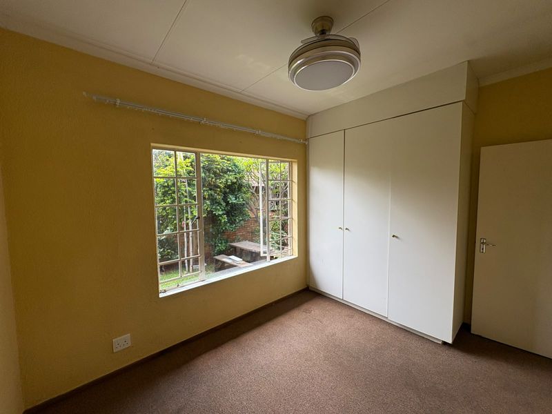 A vacant bedroom featuring built-in cupboards, a ceiling fan, and carpeted flooring with a view of the garden.
