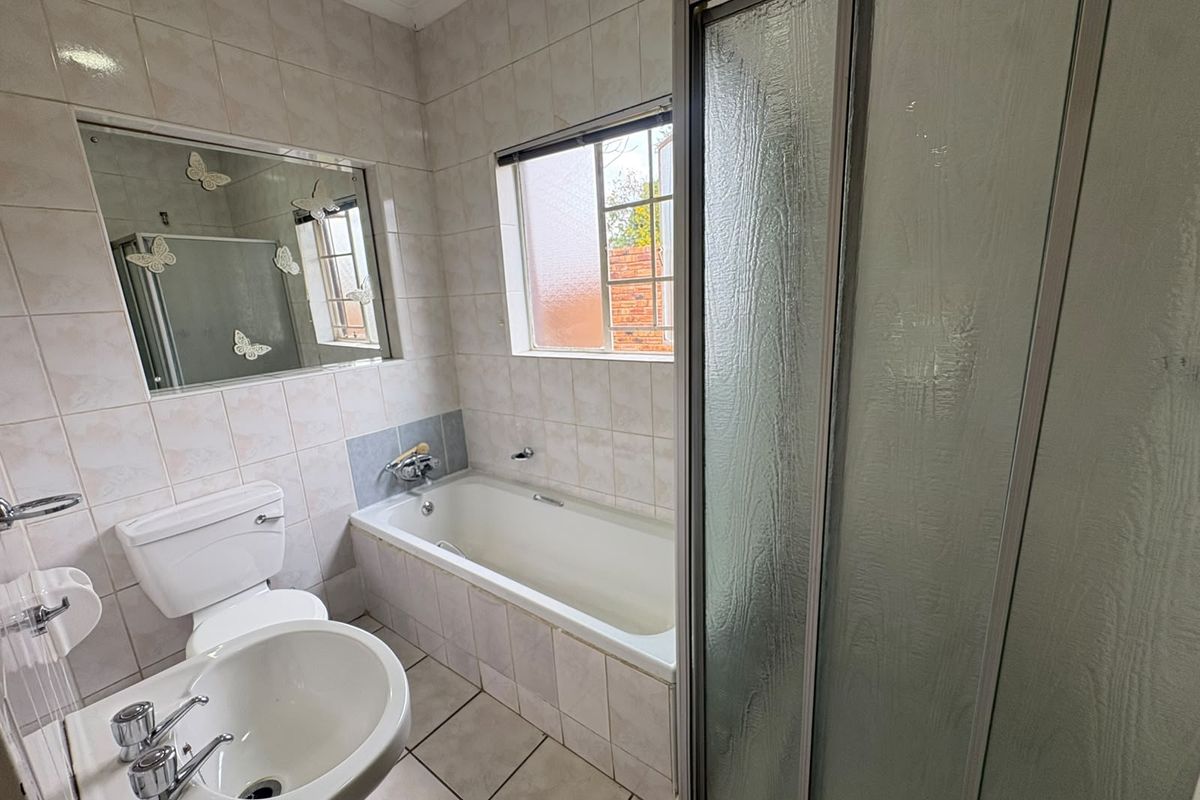 A functional bathroom featuring a built-in bathtub, separate shower enclosure, pedestal basin, and toilet with neutral wall and floor tiling.