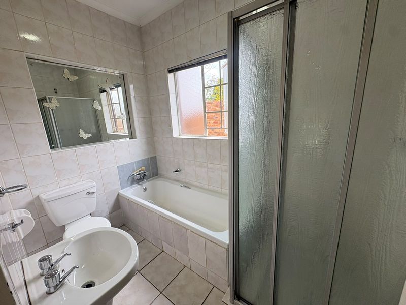 A functional bathroom featuring a built-in bathtub, separate shower enclosure, pedestal basin, and toilet with neutral wall and floor tiling.