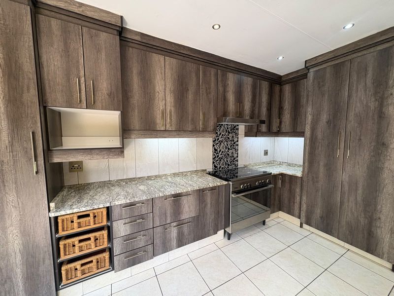 Modern kitchen featuring dark wood-look cabinetry, granite countertops, a built-in electric stove with extractor fan, and neutral tiled flooring.