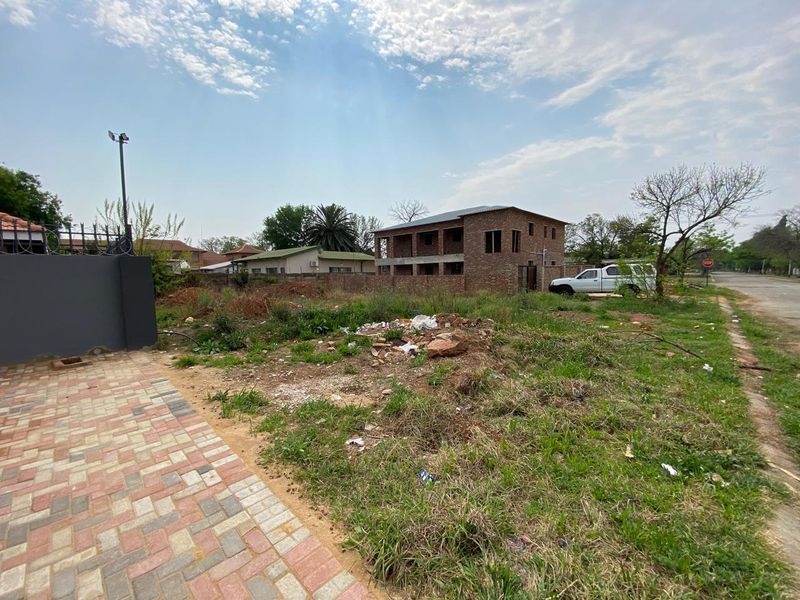 A vacant residential plot featuring a paved driveway section, perimeter walling, and security lighting, currently requiring site clearing and landscaping.