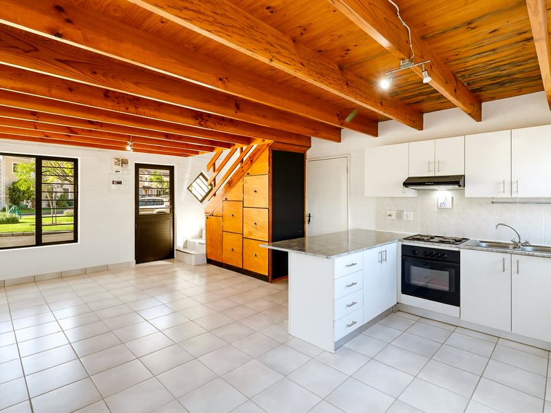 Open-plan kitchen and living area featuring exposed timber beams, tiled flooring, built-in cabinetry with granite countertops, and integrated under-stair storage.